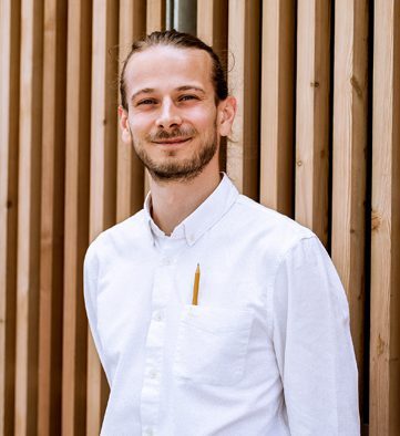 Person with a pencil in their pocket smiling at the camera.