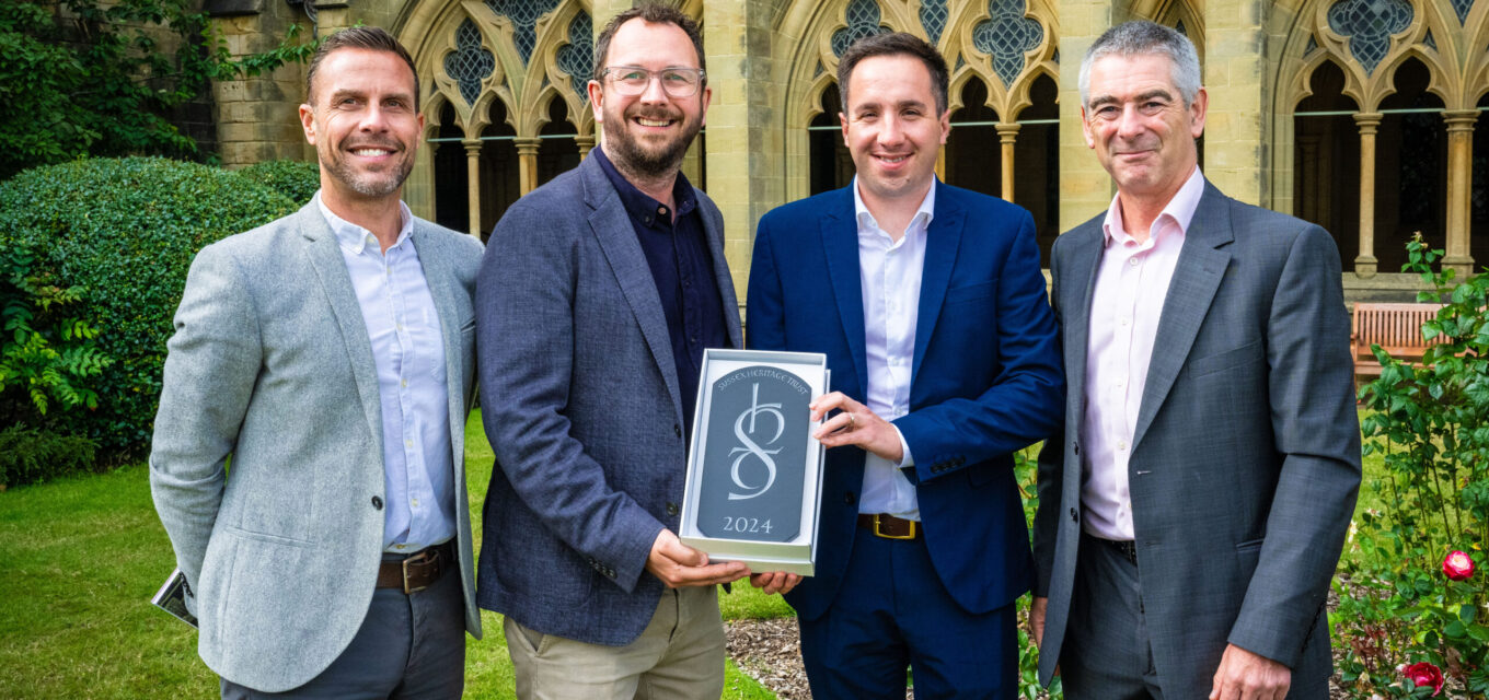 Four people in suit jackets holding an architectural award in front of an ornate church building.