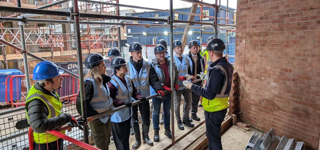 Large group of people looking at a person talking about a new site on a construction site.