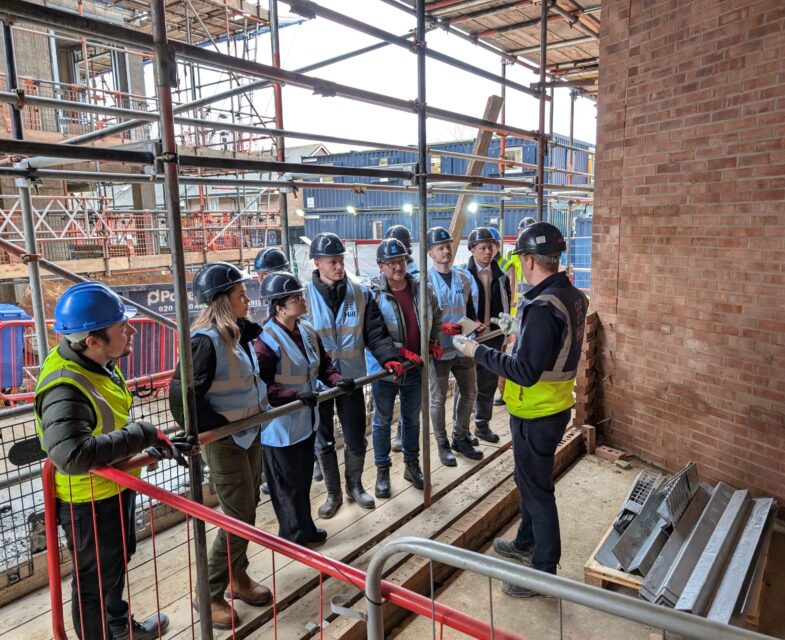 Large group of people looking at a person talking about a new site on a construction site.