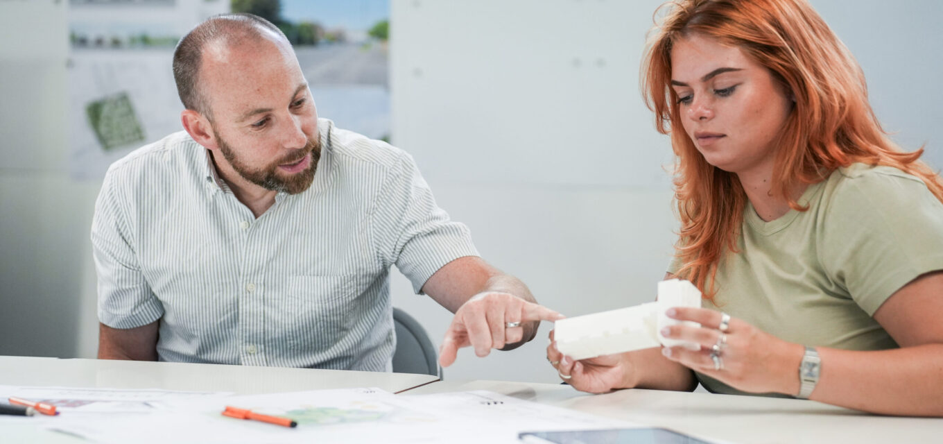 Two people discussing a 3D printed model of a residential building.