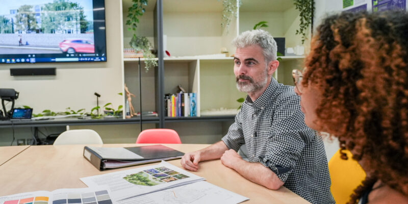 Two architects sitting around a table and facing a third person off camera, talking about an architectural project.