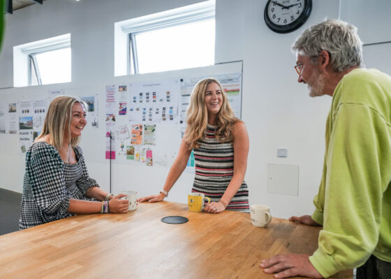 Three people standing around a kitchen island, speaking together and smiling.