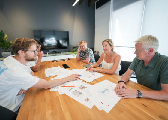 Five architectural technologists discussing technical drawings inside a meeting room.