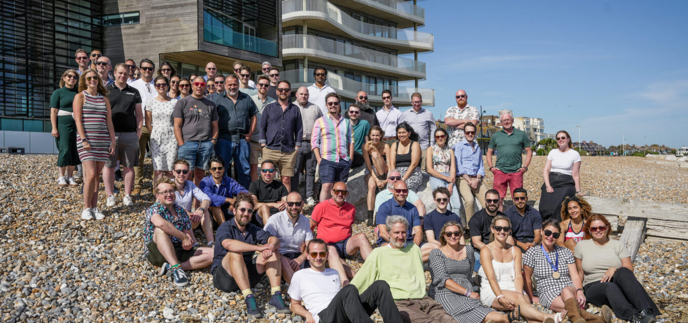 Large group of people on the beach in front of a tall residential building, all looking at the camera.