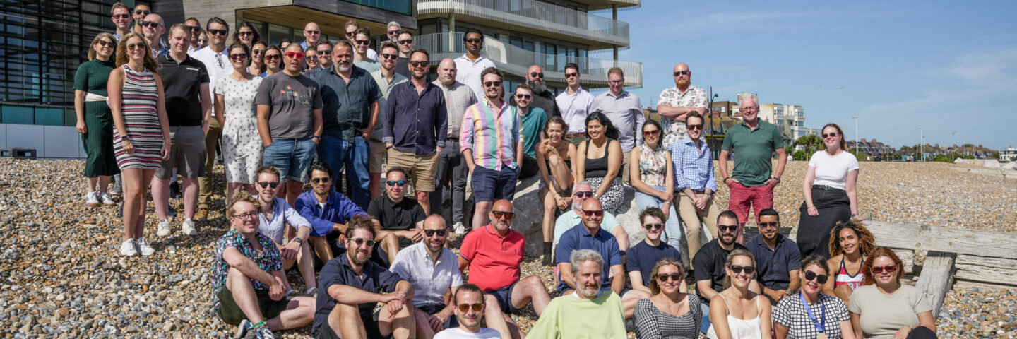 Large group of people on the beach in front of a tall residential building, all looking at the camera.