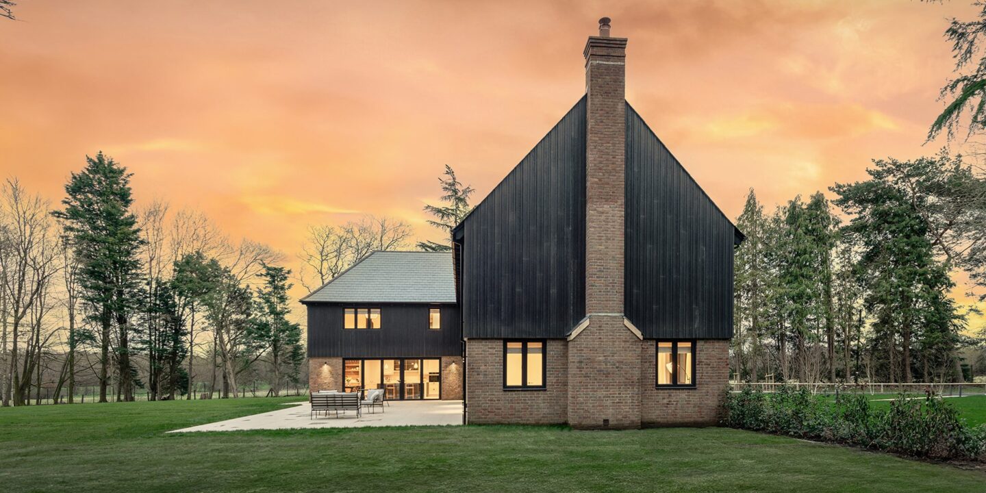 Red brick residential house with large chimney and black timber cladding at sunset.