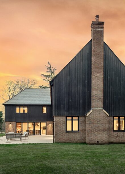 Red brick residential house with large chimney and black timber cladding at sunset.