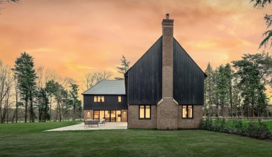 Red brick residential house with large chimney and black timber cladding at sunset.