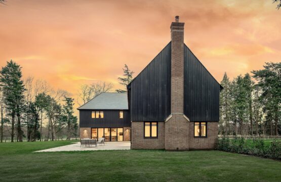 Red brick residential house with large chimney and black timber cladding at sunset.
