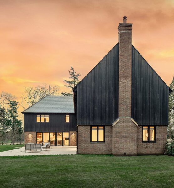 Red brick residential house with large chimney and black timber cladding at sunset.