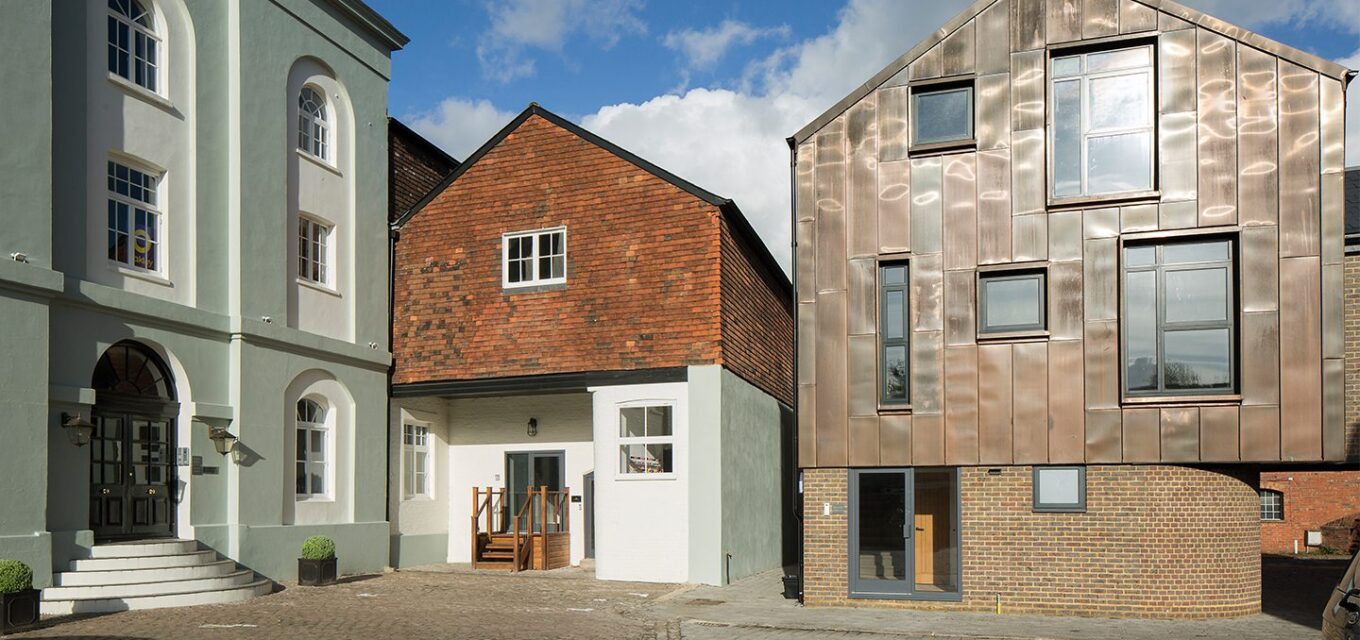 Courtyard with three buildings of different styles, one traditional, one more contemporary and one in metal cladding inspired by the traditional house shapes.