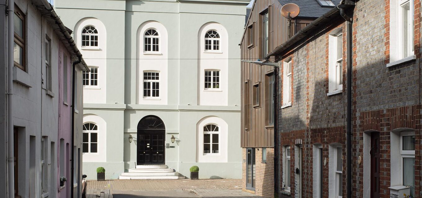 Rendered building with arched windows and details at the end of a street lined with both traditional and contemporary buildings.