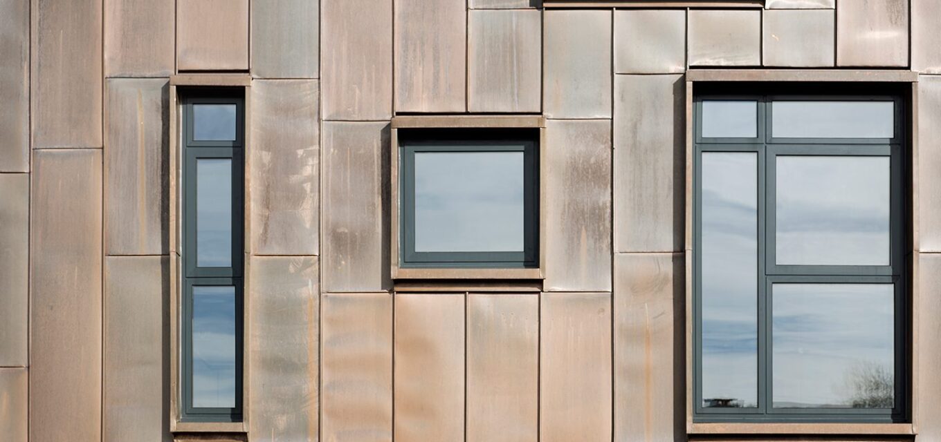 Metal clad exterior wall with three windows all of different sizes.