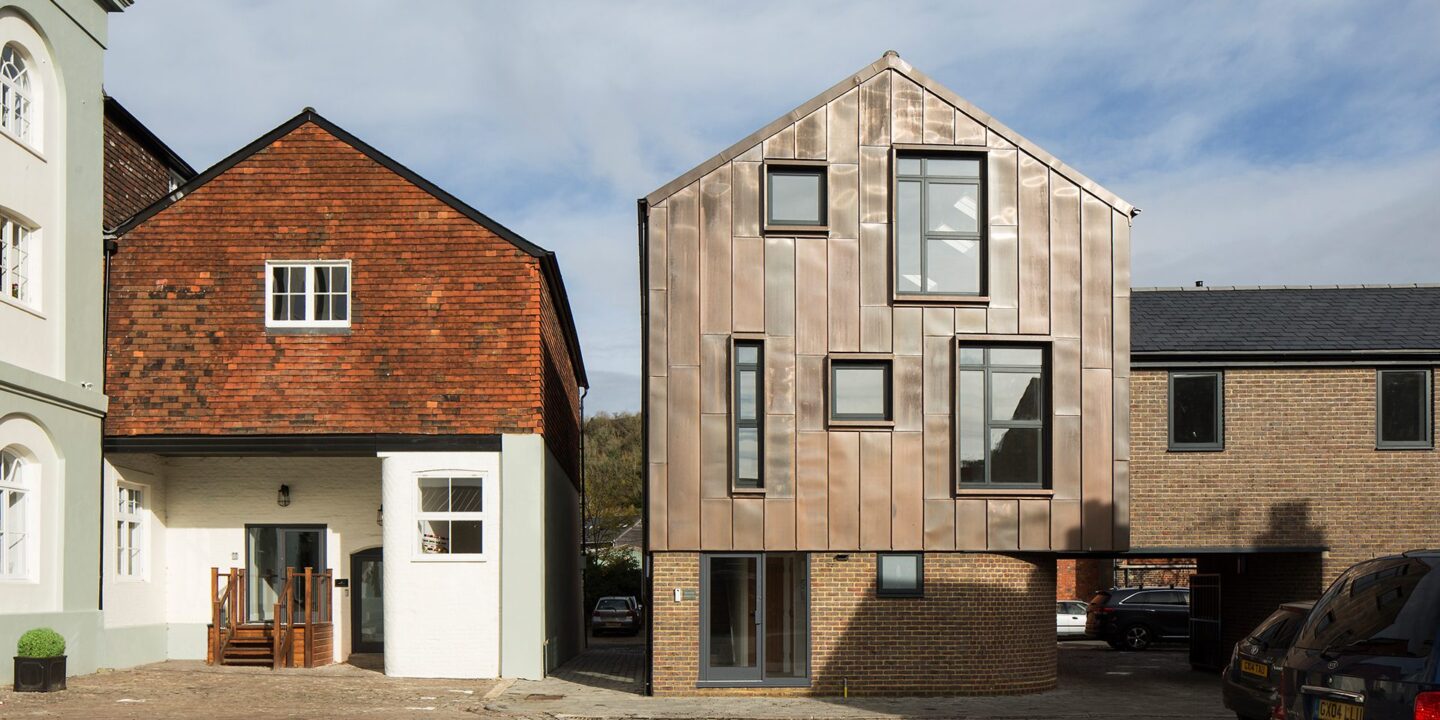 Contemporary residential building with metal cladding and a curved bottom wall sitting next to a traditional house with the same roof line.