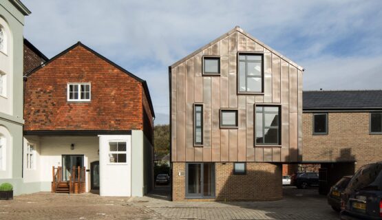 Contemporary residential building with metal cladding and a curved bottom wall sitting next to a traditional house with the same roof line.