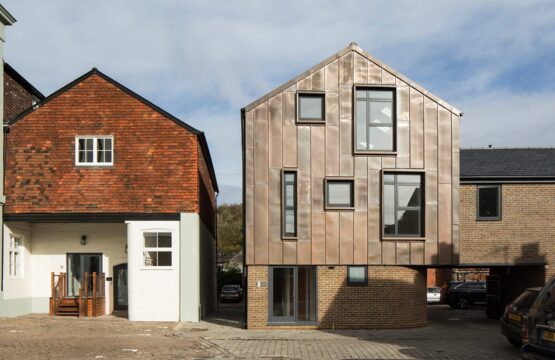 Contemporary residential building with metal cladding and a curved bottom wall sitting next to a traditional house with the same roof line.