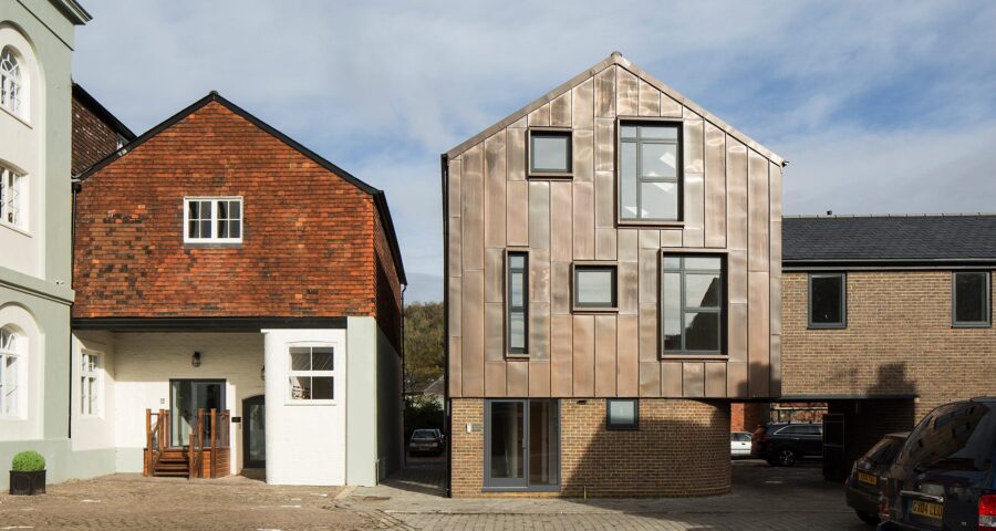 Contemporary residential building with metal cladding and a curved bottom wall sitting next to a traditional house with the same roof line.