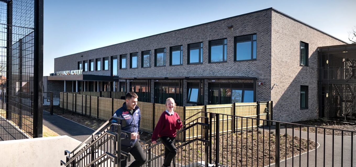 Two students walking up external stair case in front of a brick school building in a contemporary style.