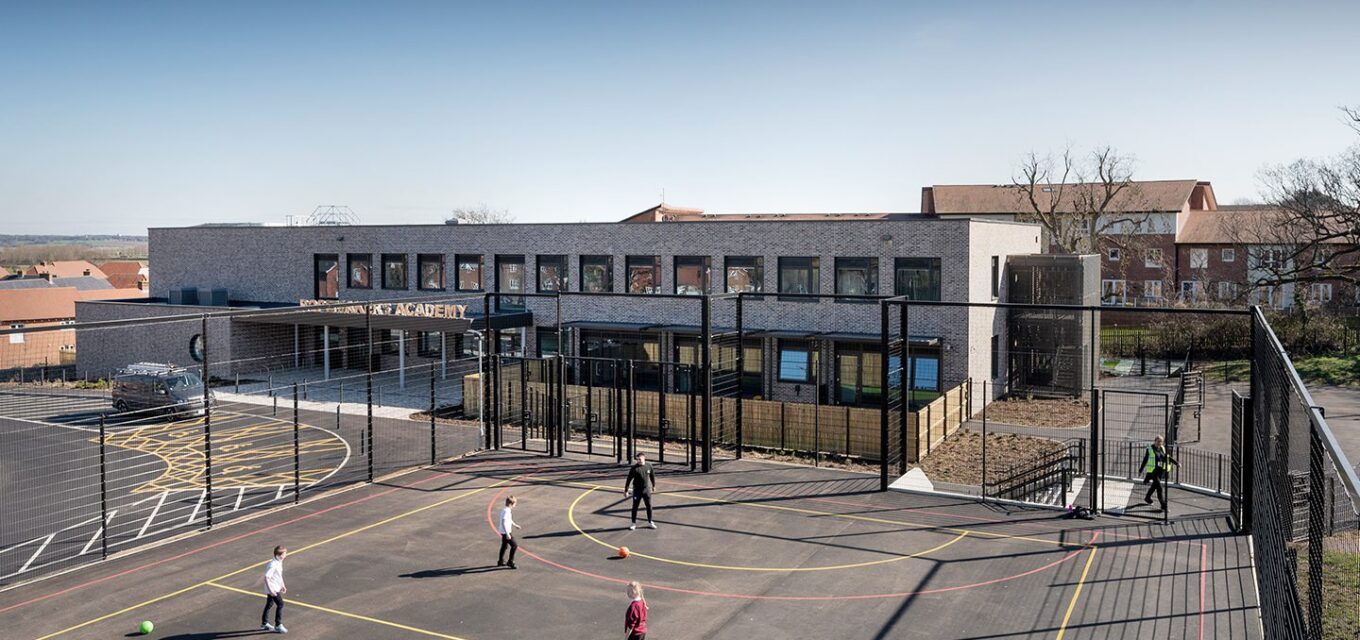 Multi-use games area with children playing sports in front of a contemporary brick secondary school.