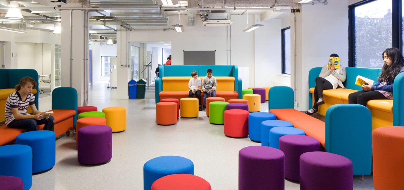 Student area with colourful sofas and stools, with five students sitting and reading in books.
