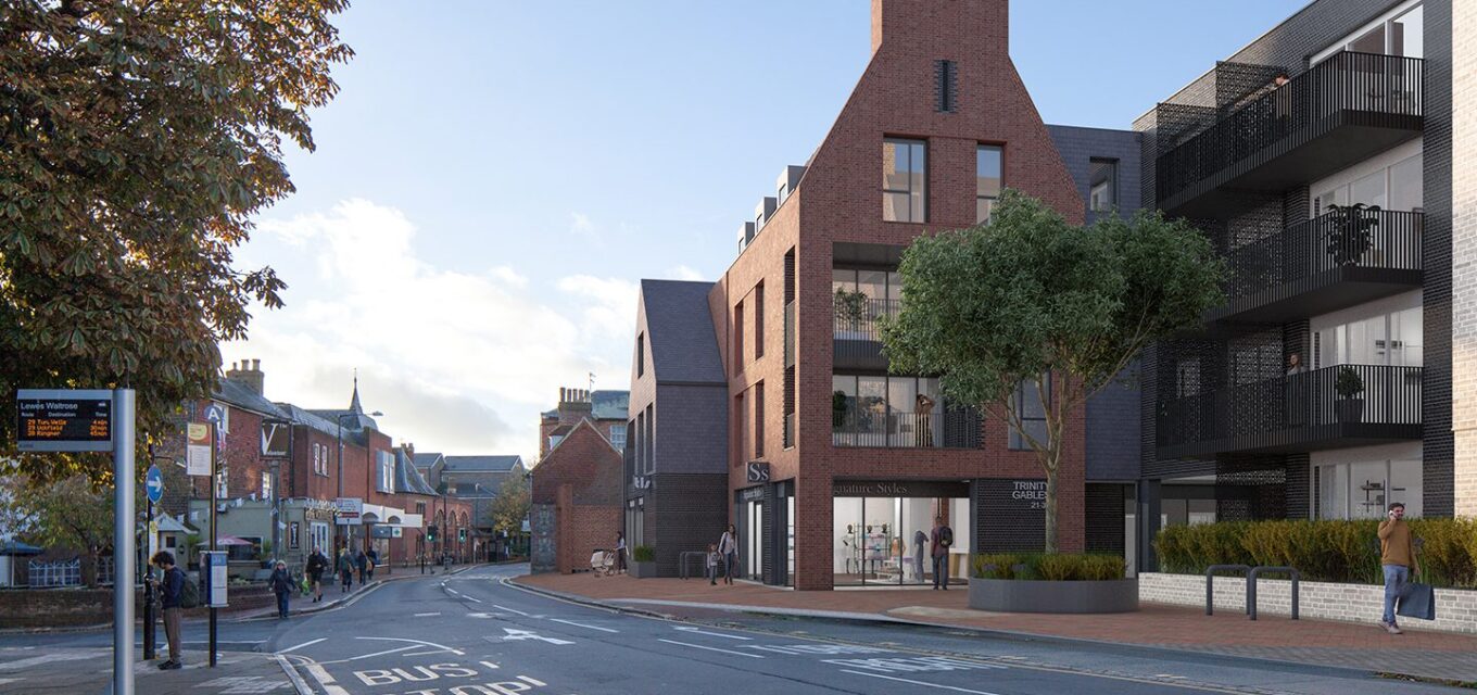 Red brick contemporary building with a gable and inset balconies with a bus stop across the road.