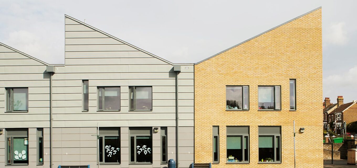 Contemporary school building with two sections with angled roof line and grey cladding and yellow brick.