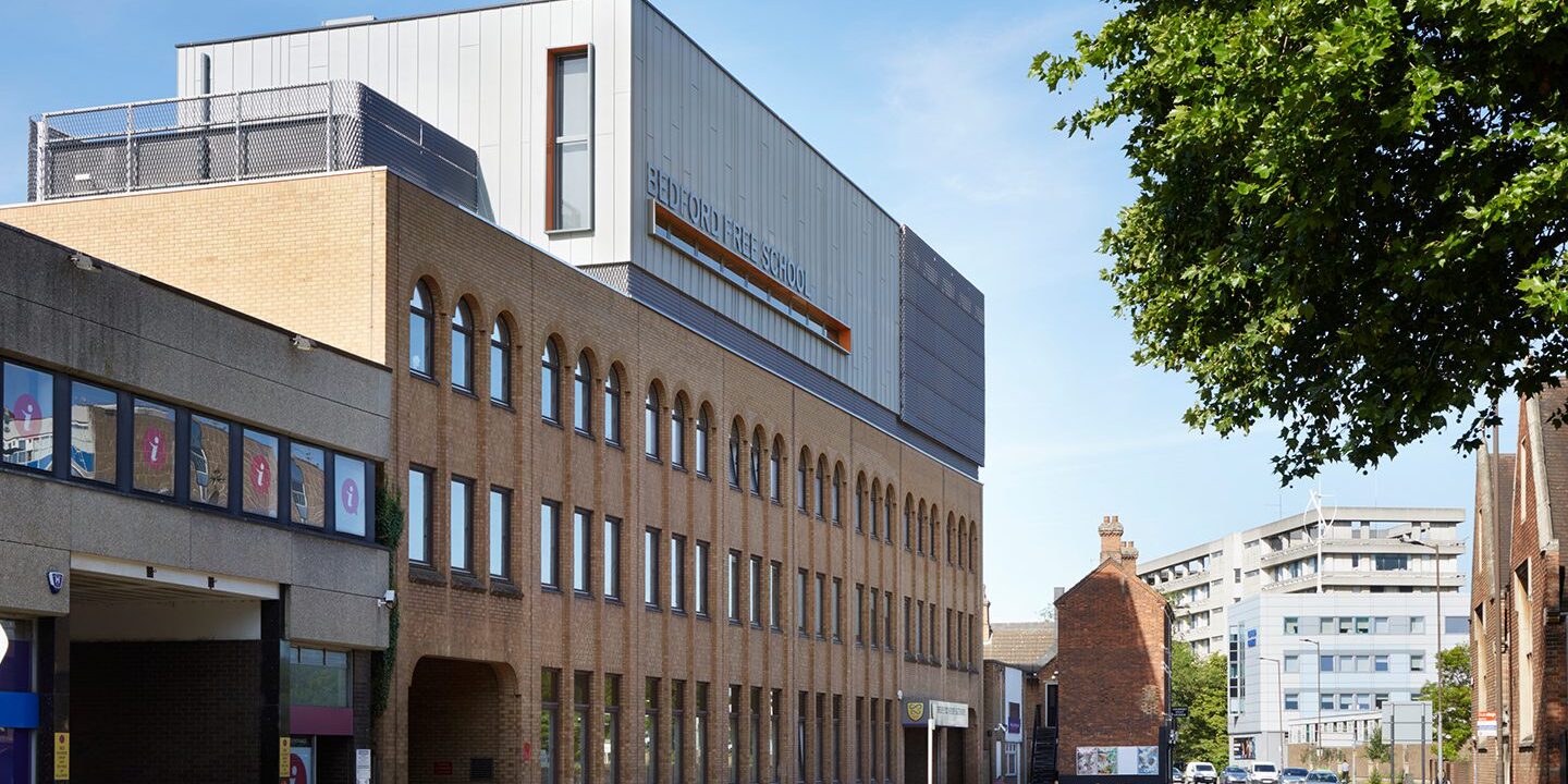 Brick clad school building with metal clad roof extension looking like a box with orange-detail windows.