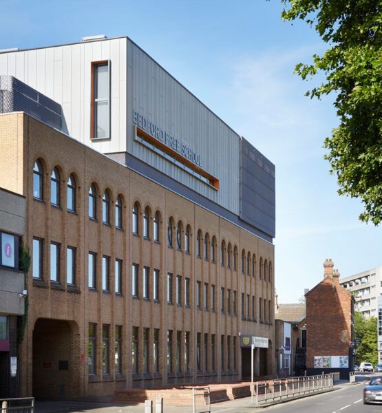 Brick clad school building with metal clad roof extension looking like a box with orange-detail windows.