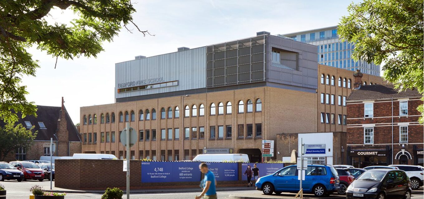 Traditional brick school building with arched windows and metal clad roof extension with metal mesh.