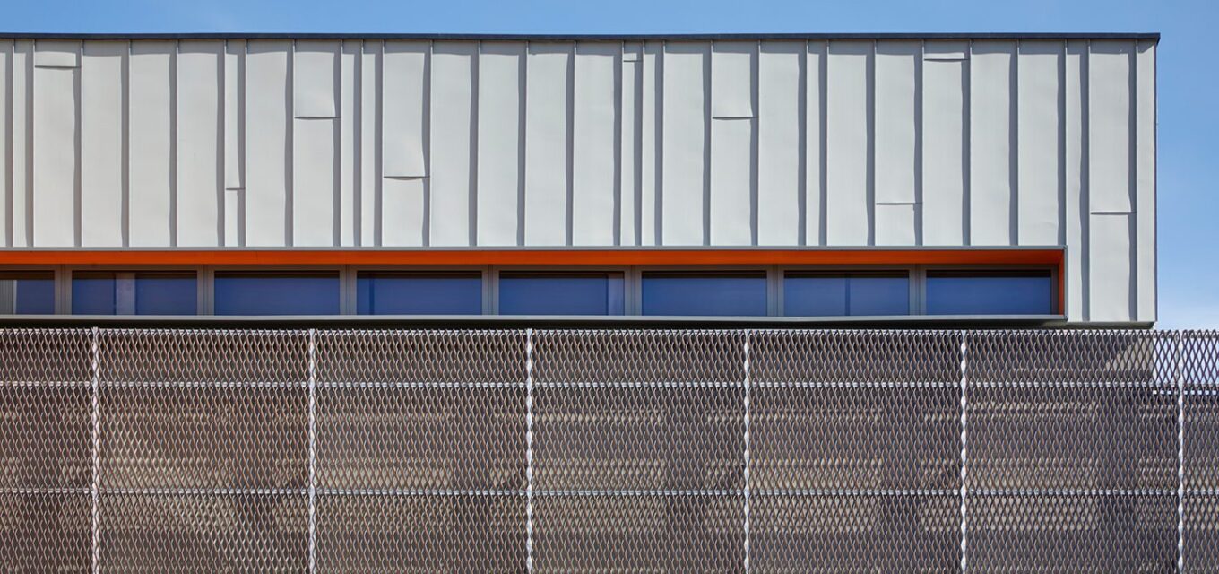 Metal cladded angled building with flat roof and long wide windows with orange wind surround