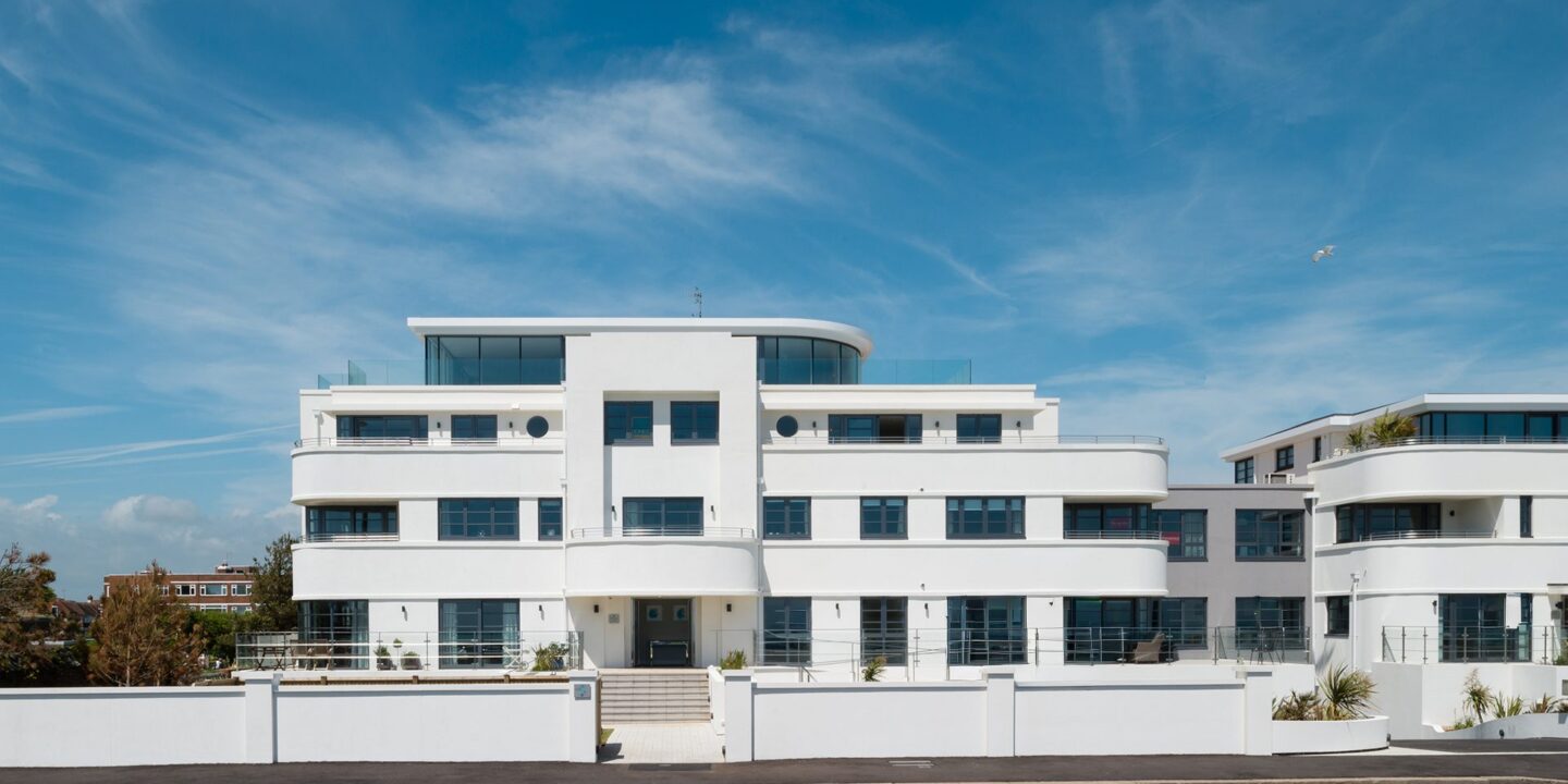 White Art Deco-style flat building with glazed top floor and roof terrace, curved balconies and white rendered front wall
