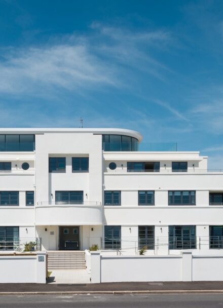 White Art Deco-style flat building with glazed top floor and roof terrace, curved balconies and white rendered front wall