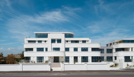 White Art Deco-style flat building with glazed top floor and roof terrace, curved balconies and white rendered front wall