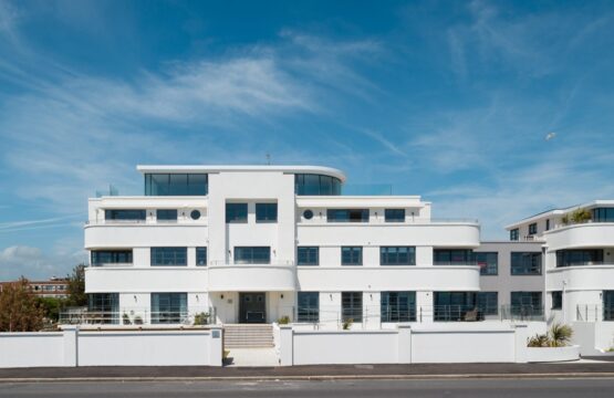 White Art Deco-style flat building with glazed top floor and roof terrace, curved balconies and white rendered front wall