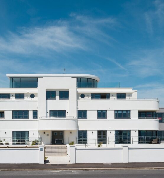 White Art Deco-style flat building with glazed top floor and roof terrace, curved balconies and white rendered front wall