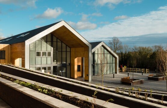 Two large school buildings in a barn-style with large glazed fronts and paved front area with trees and plants in a rural setting