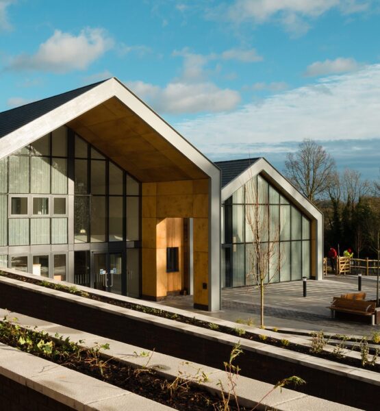 Two large school buildings in a barn-style with large glazed fronts and paved front area with trees and plants in a rural setting