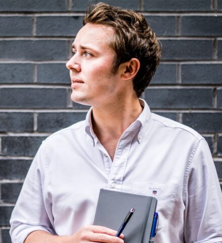 Person holding a notebook and a pencil smiling at the camera.