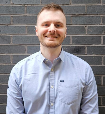 Person standing in front of a grey brick wall smiling at the camera.