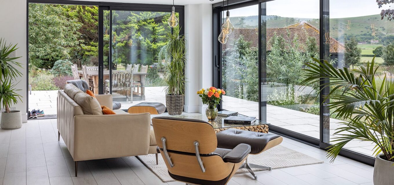 A lounge with a sofa, arm chair and coffee table with large floor-to-ceiling windows overlooking a garden