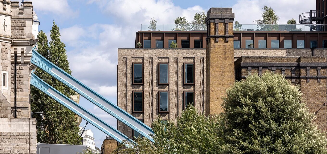 Mixed-use building with brick and metal cladding details, behind a blue metal beam of the Tower Bridge.