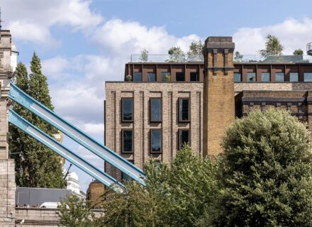Mixed-use building with brick and metal cladding details, behind a blue metal beam of the Tower Bridge.