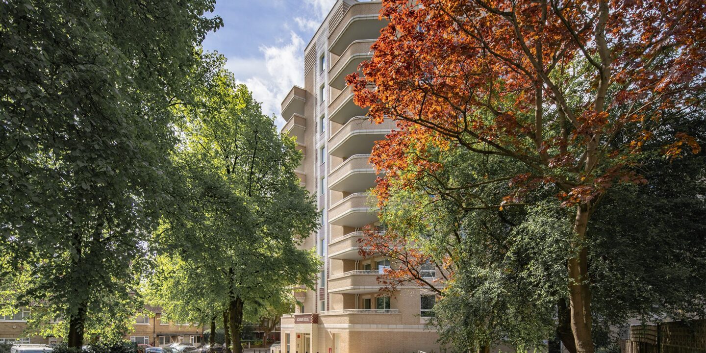 Two trees with green and orange leaves in front of an Art Deco style brick residential building entrance