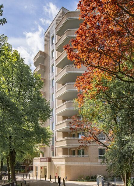 Two trees with green and orange leaves in front of an Art Deco style brick residential building entrance