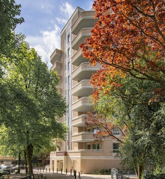Two trees with green and orange leaves in front of an Art Deco style brick residential building entrance