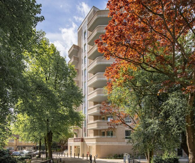 Two trees with green and orange leaves in front of an Art Deco style brick residential building entrance