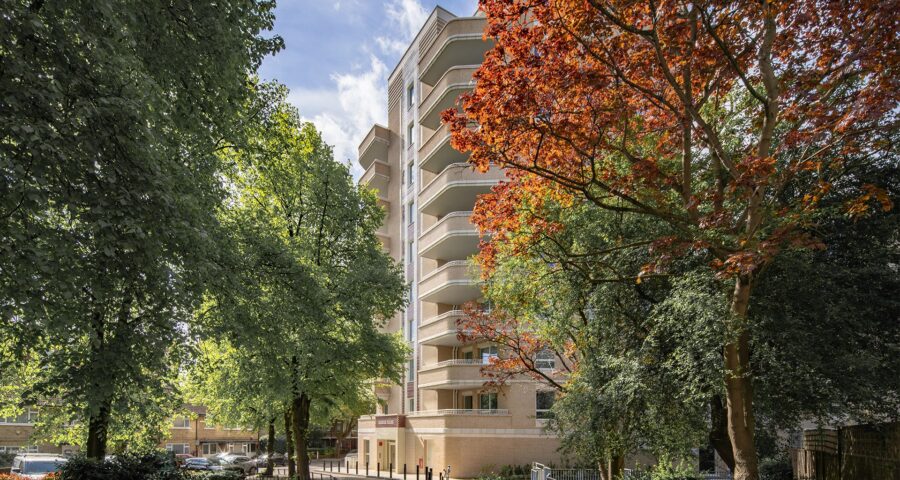 Two trees with green and orange leaves in front of an Art Deco style brick residential building entrance