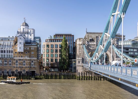 Brick and metal cladded building with reflective windows with the River Thames and Tower Bridge in front.