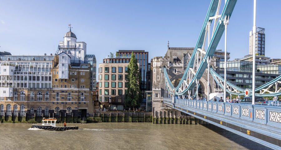 Brick and metal cladded building with reflective windows with the River Thames and Tower Bridge in front.